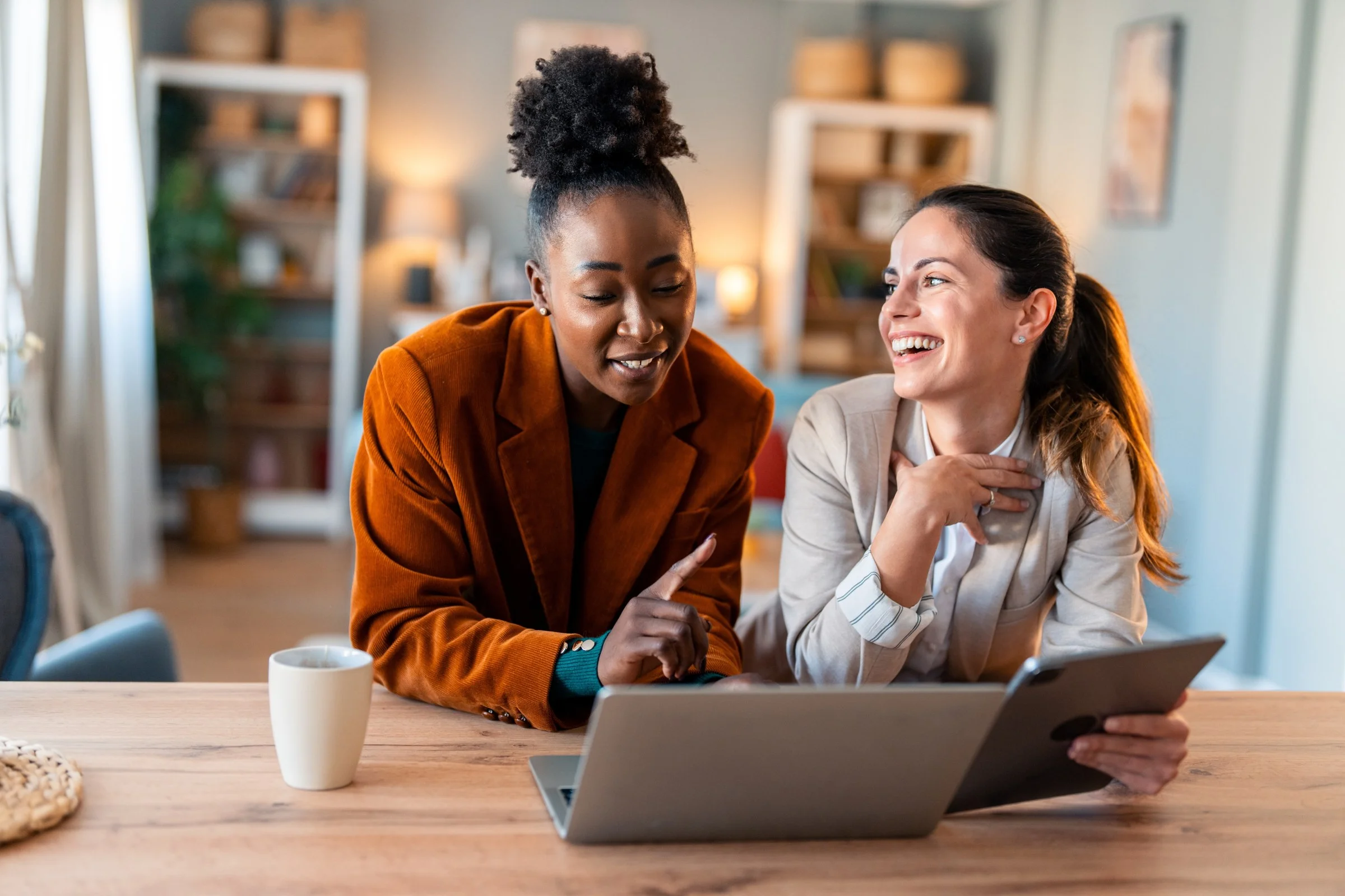Two colleagues laughing over a laptop and tablet